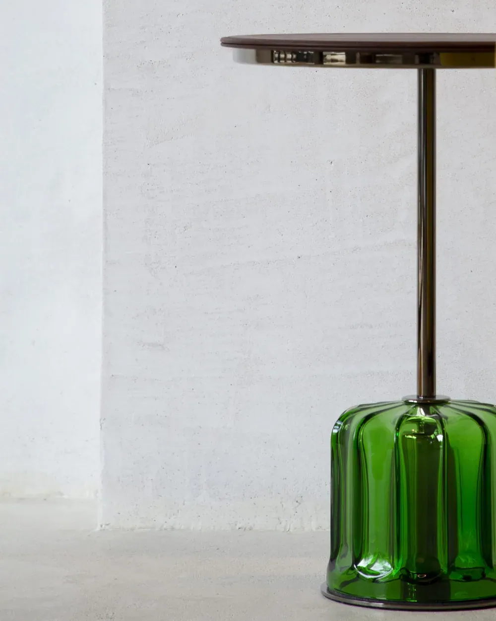 A green glass pendant lamp hanging against a white wall in the showroom.